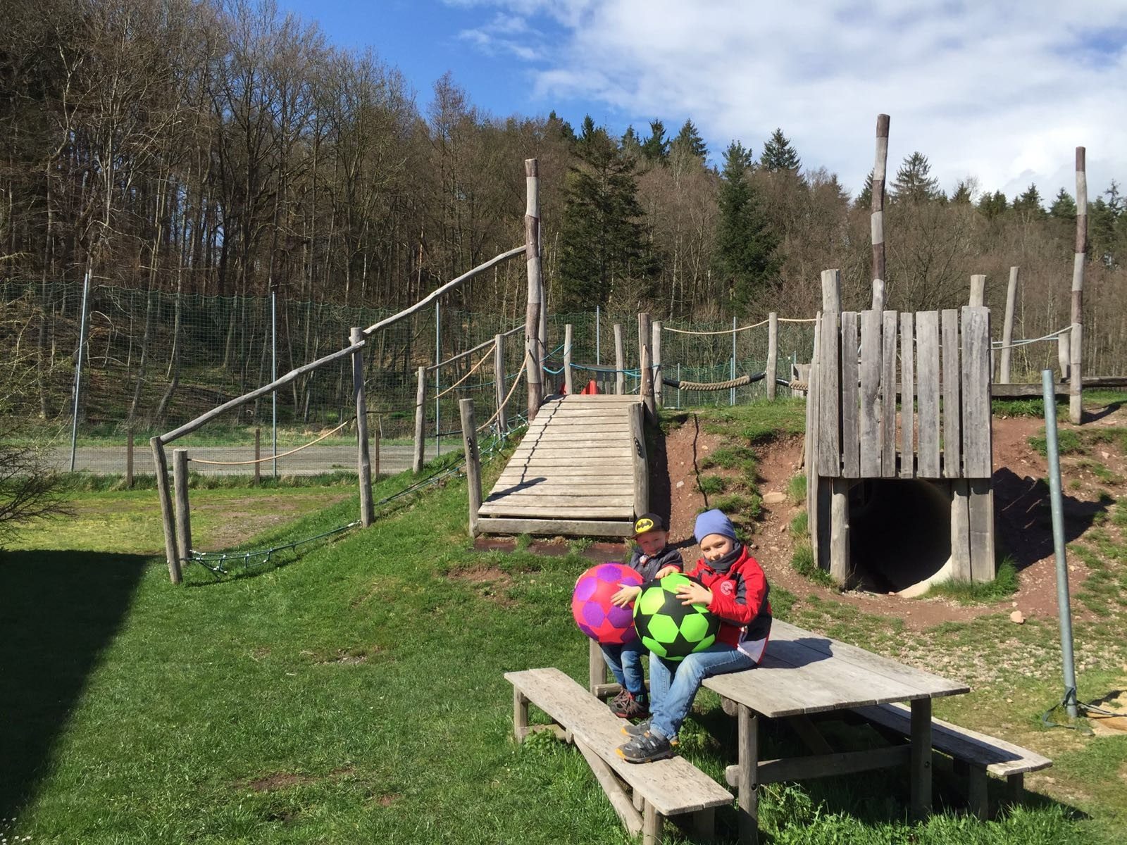 Kind sitzt mit bunten Bällen auf dem Holzspielplatz des Horts